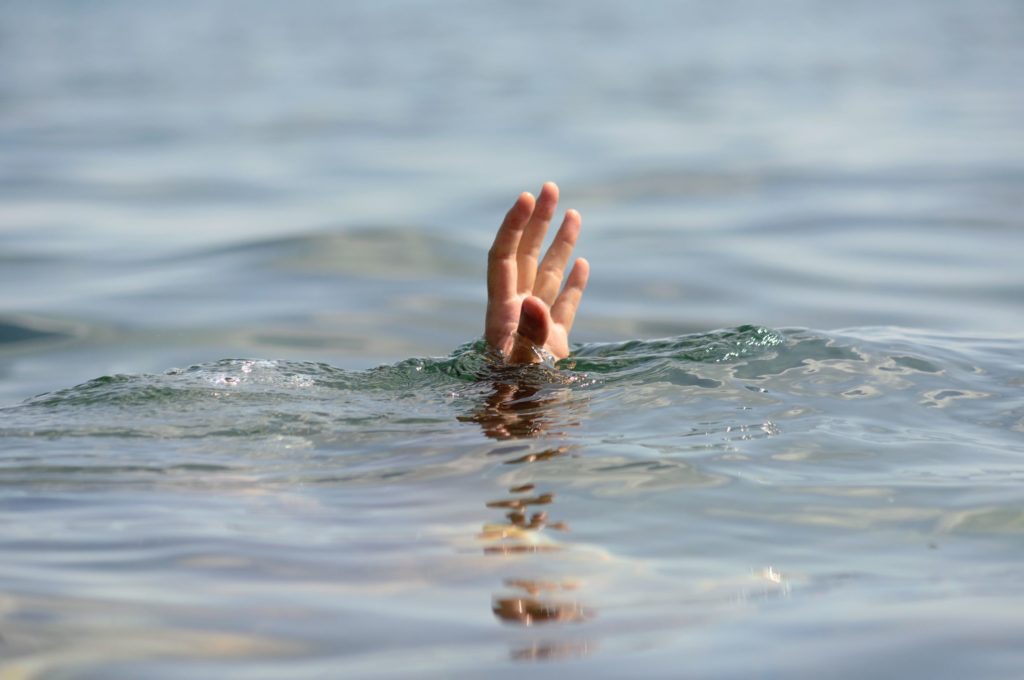 Person underwater reaches out hand about the surface